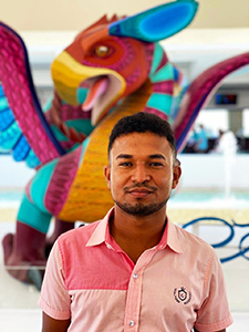 Bearded, Afro-Mexican young man in a pink shirt in front of a colorful bird sculpture