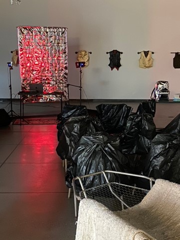 A still image of the pre-event set-up at Contemporary Craft in Lawrenceville. Seats are covered in black trash bags and face a metallic backdrop that is lit in red light.